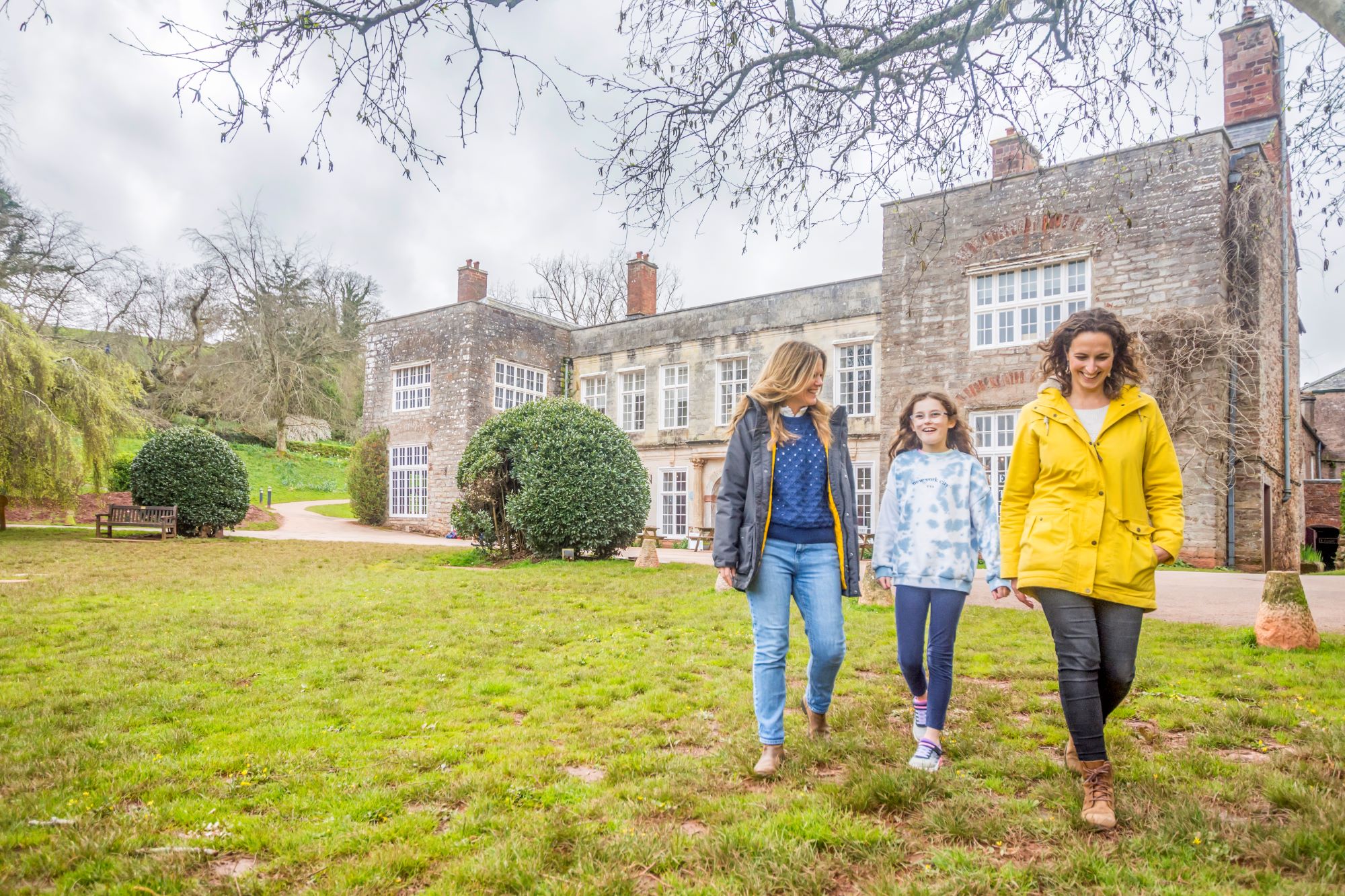 Two women and a child walking in front of Cockington Court's manor house.