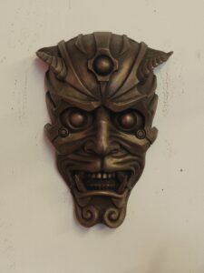 Summer Sculpture Trail 2026 A Bronze Mask Hung On A Wall. The Style Of The Mask Is Sci-Fi With Robotic Features Around It'S Head.